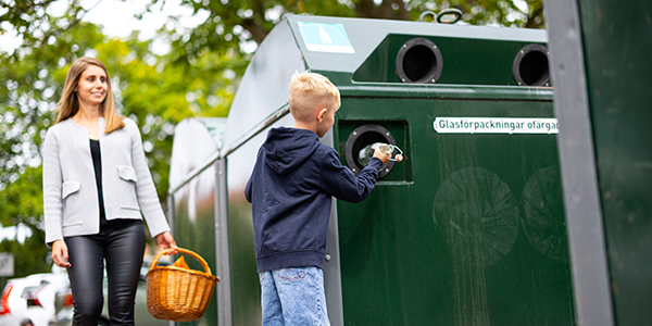 Kvinna och pojke lämnar förpackningar i en behållare på återvinningsstationen. Foto: Avfall Sverige