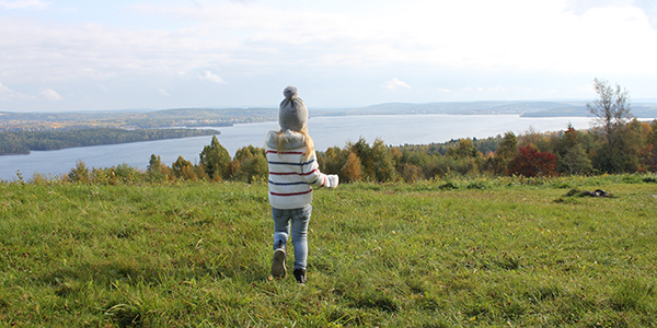 Flicka står på en högt belägen äng och blickar ut över en sjö. Foto: Julianna Heij Laurentz